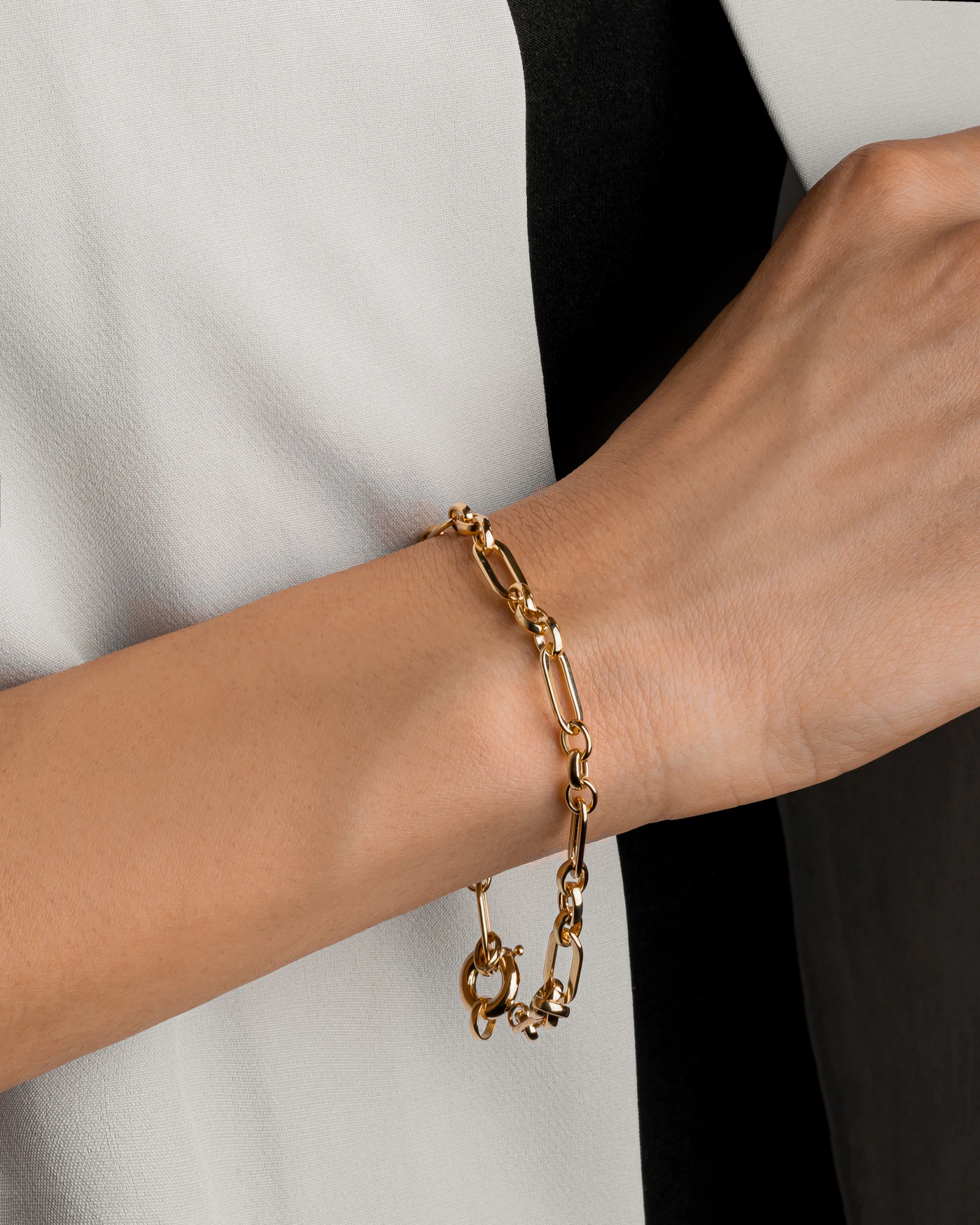 Gold-coloured chain bracelet worn with a white sleeve