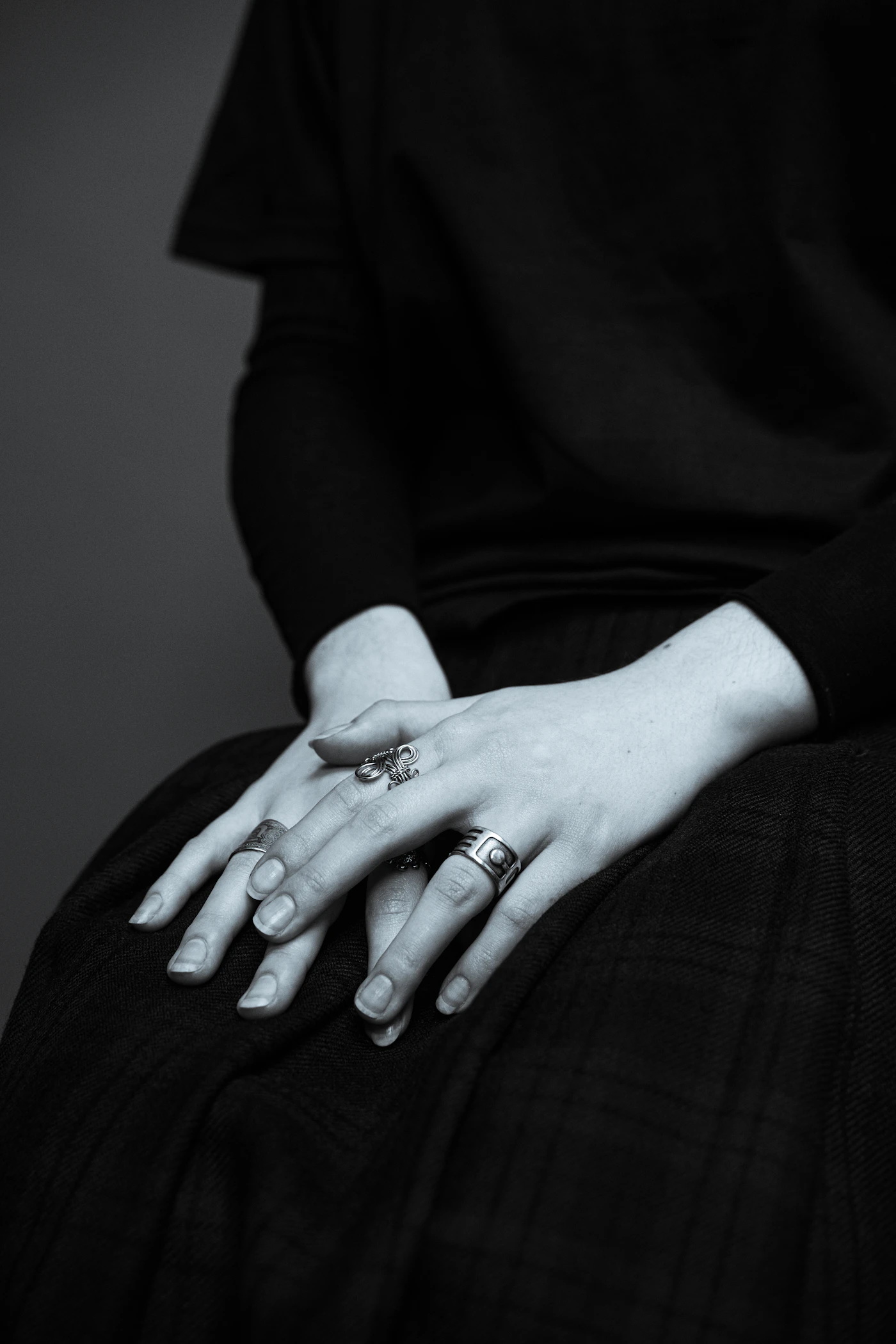 Crossed hands wearing rings against a black outfit