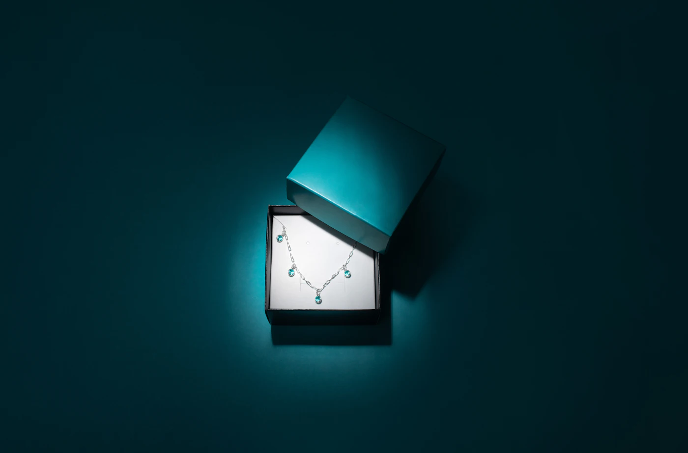 Open jewellery gift box on a dark turquoise background