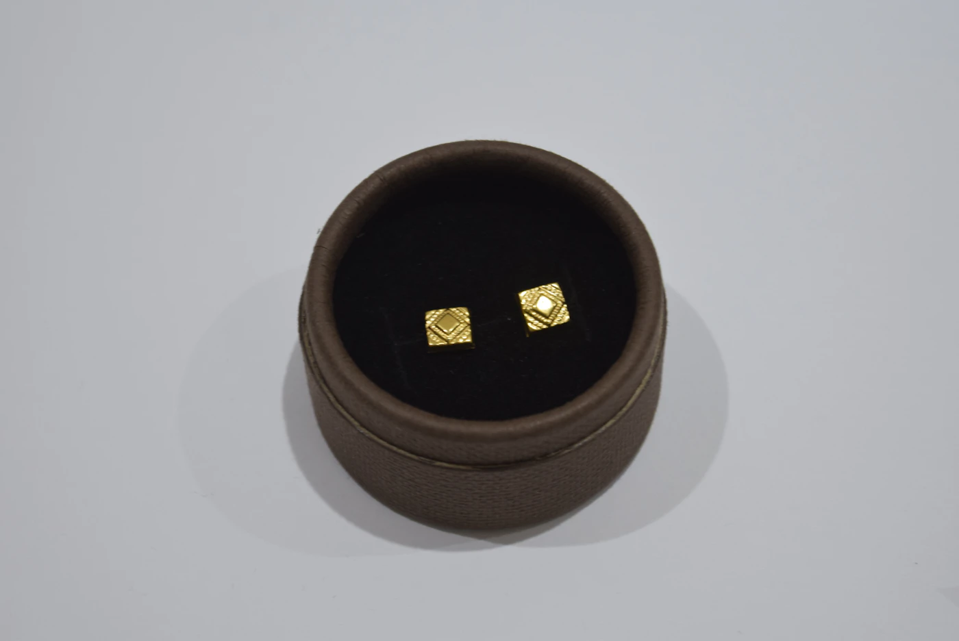Pair of small gold-coloured stud earrings in a round box