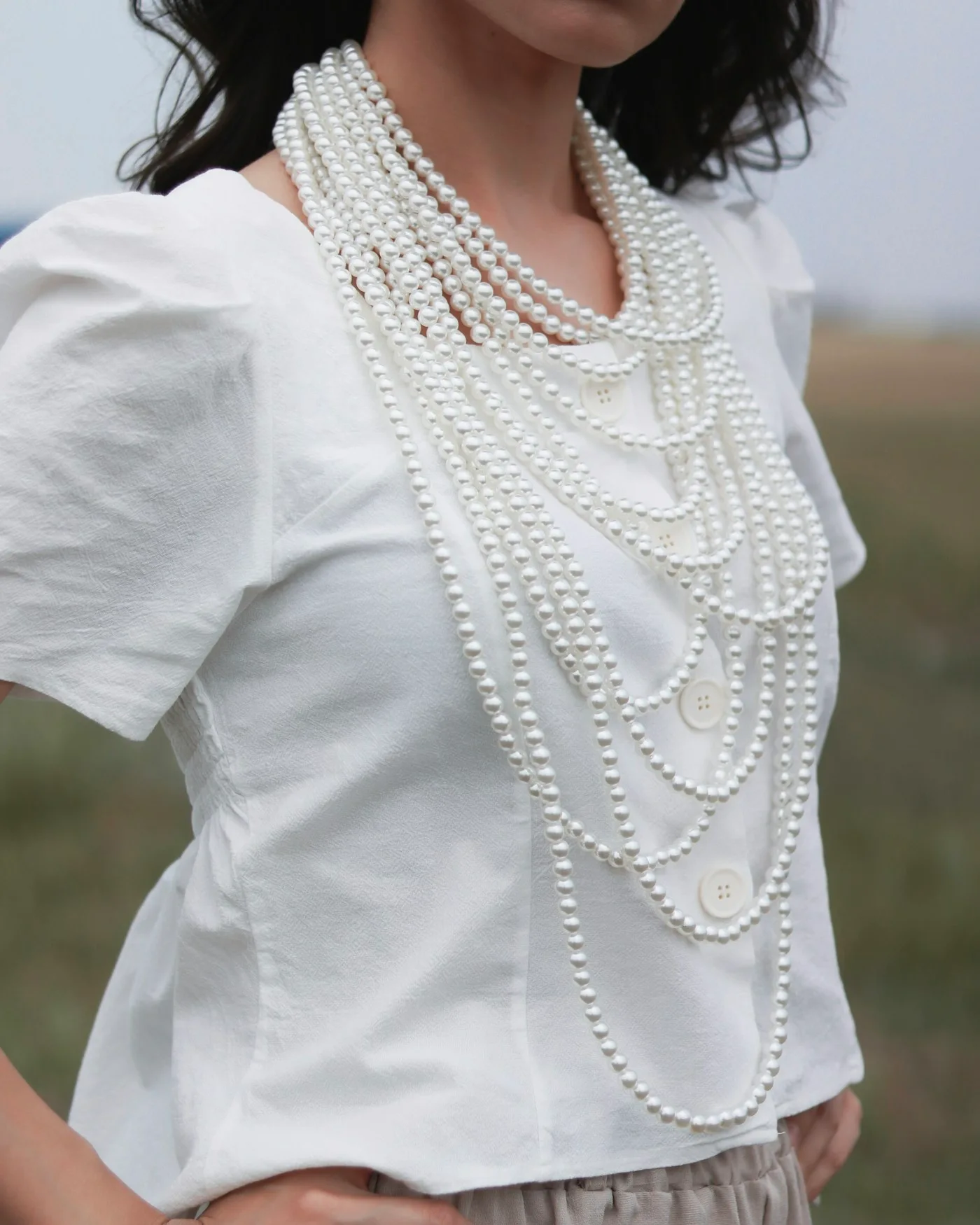 Woman styling a white pearl necklace with a white blouse