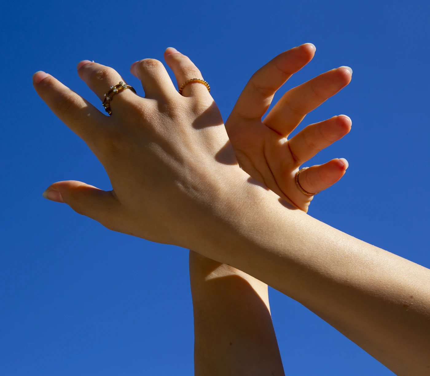 Hands wearing rings against a bright blue sky