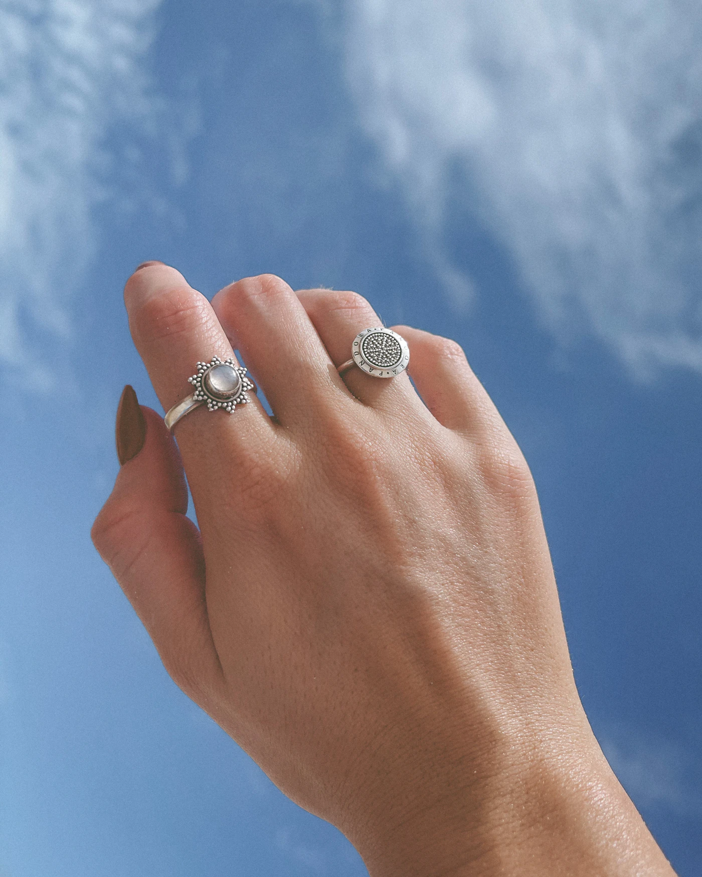 Hand wearing silver-coloured rings beneath a cloudy sky