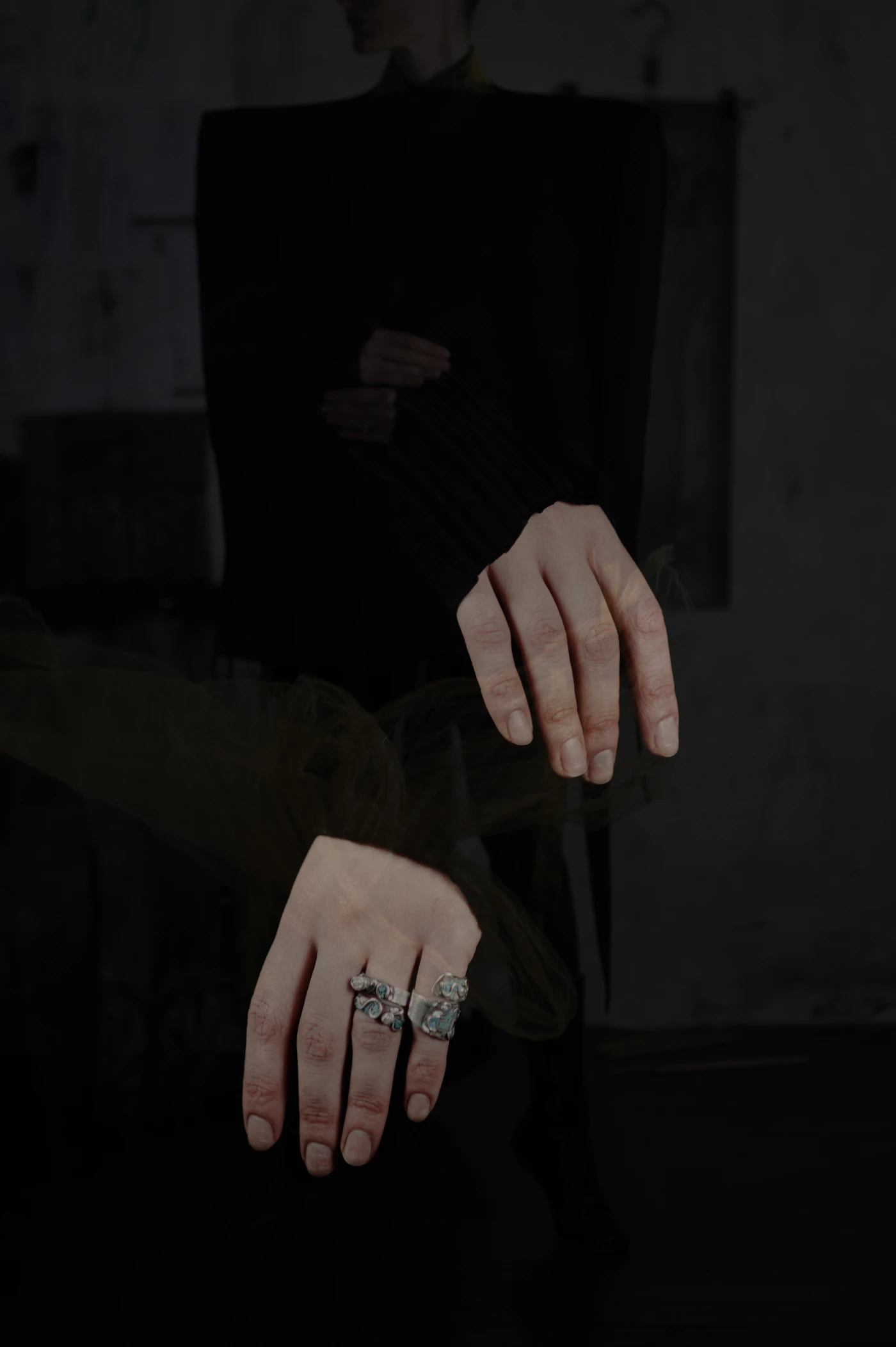 Hands wearing rings against dark clothing